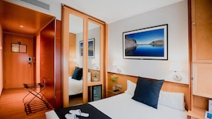 A hotel room with a bed, a bedside table, a mirror, a wall-mounted picture, and a wooden wardrobe.