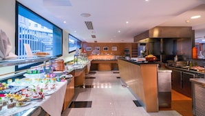 A buffet setup with various food items and beverages, a kitchen area with stainless steel appliances, and a large window with a view of buildings.