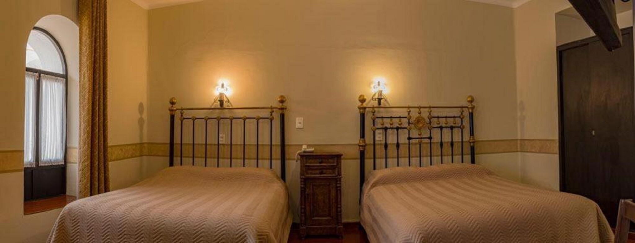 Une chambre avec deux lits, une petite table de chevet en bois et une fenêtre avec des rideaux.