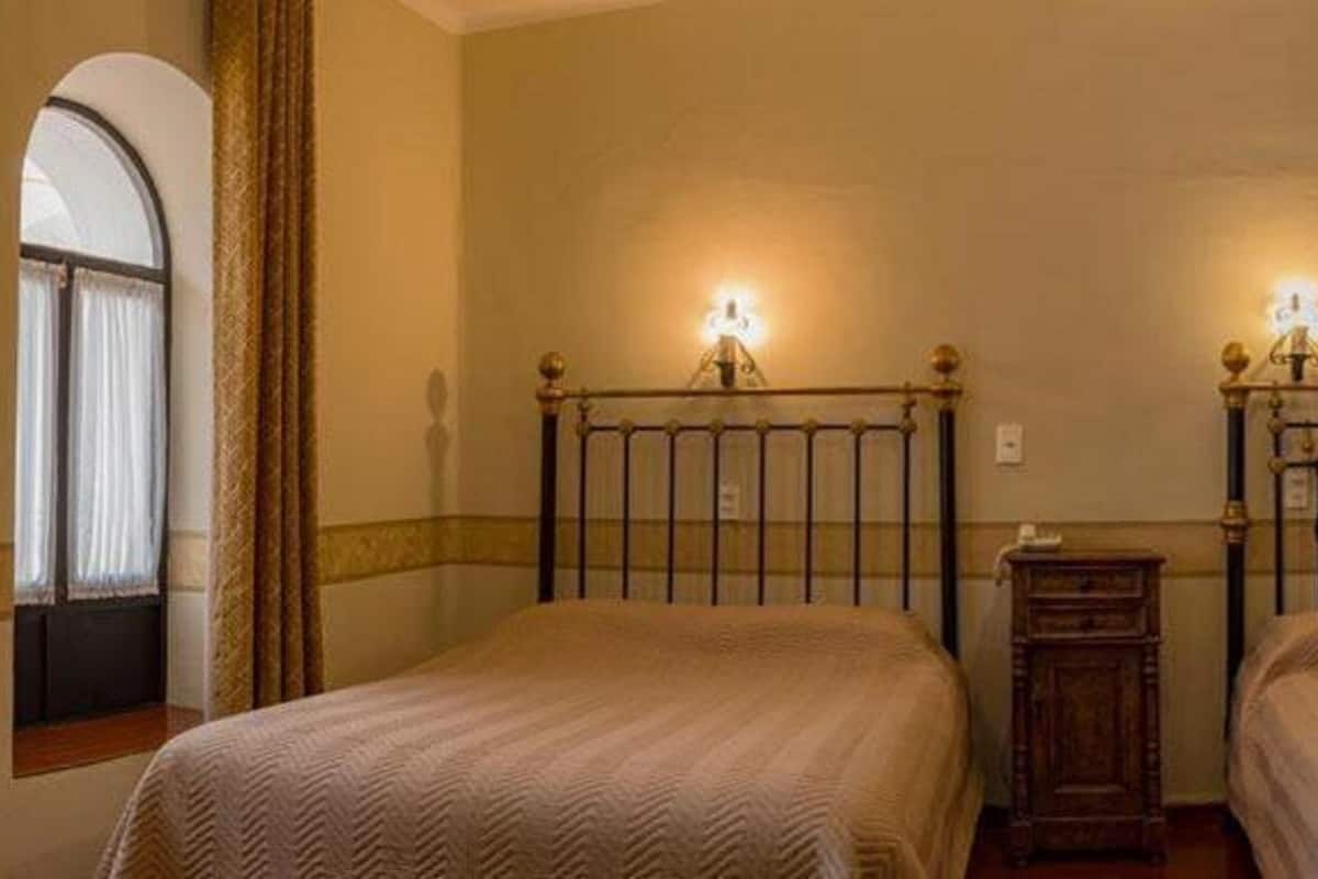 A room with two beds, a small wooden nightstand, and a window with curtains.
