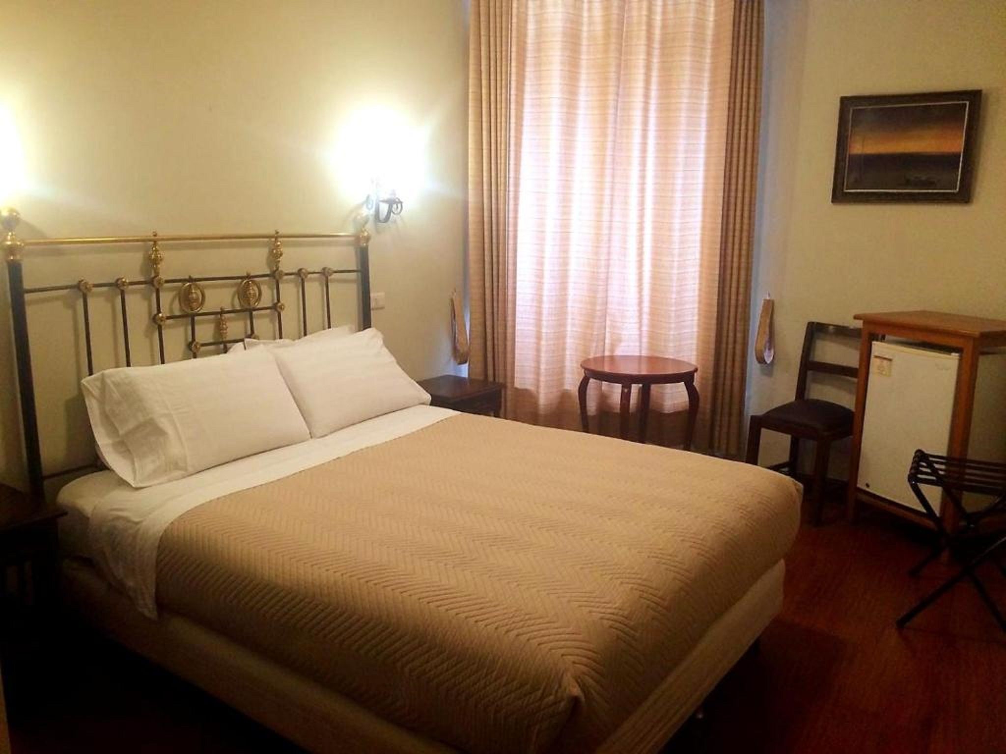 Habitación de hotel con cama, escritorio, silla, mesita y ventana con cortinas.