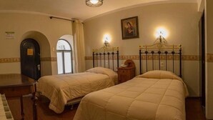 A hotel room with two beds, a piano, a door, and a painting on the wall. - Colonial Hostal (Potosi)