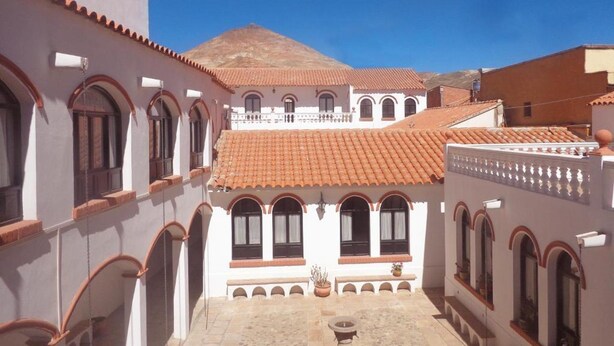A courtyard with white buildings, red-tiled roofs, and arched windows. - Colonial Hostal (Potosi)