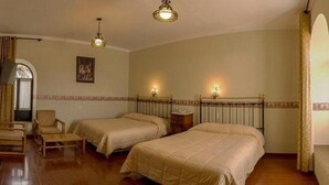 A hotel room with two beds, a chair, a radiator, a mirror, and a chandelier. - Colonial Hostal (Potosi)