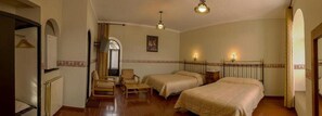 A hotel room with two beds, a chair, a radiator, a mirror, and a chandelier. - Colonial Hostal (Potosi)