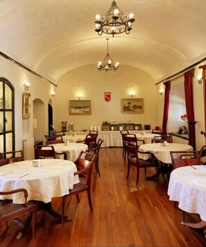 A dining area with round tables, chairs, a chandelier, and a wooden floor. - Colonial Hostal (Potosi)