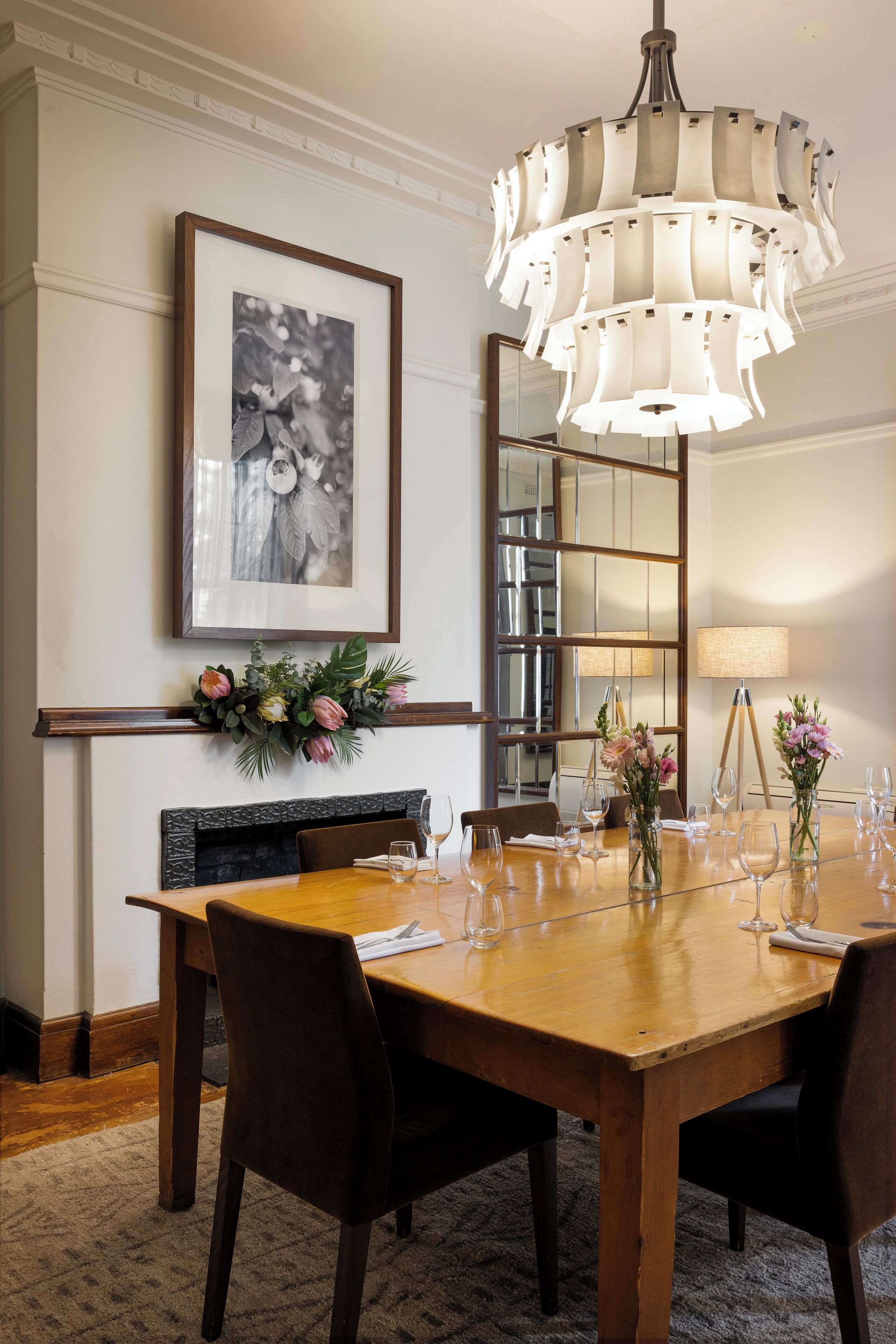 Un coin repas avec une table en bois, des chaises, un lustre, une cheminée et un tableau encadré au mur.