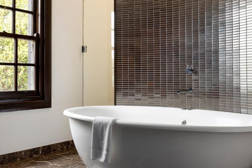A modern bathroom with a freestanding bathtub, a window with a view of greenery, and a shower area with a tiled wall.