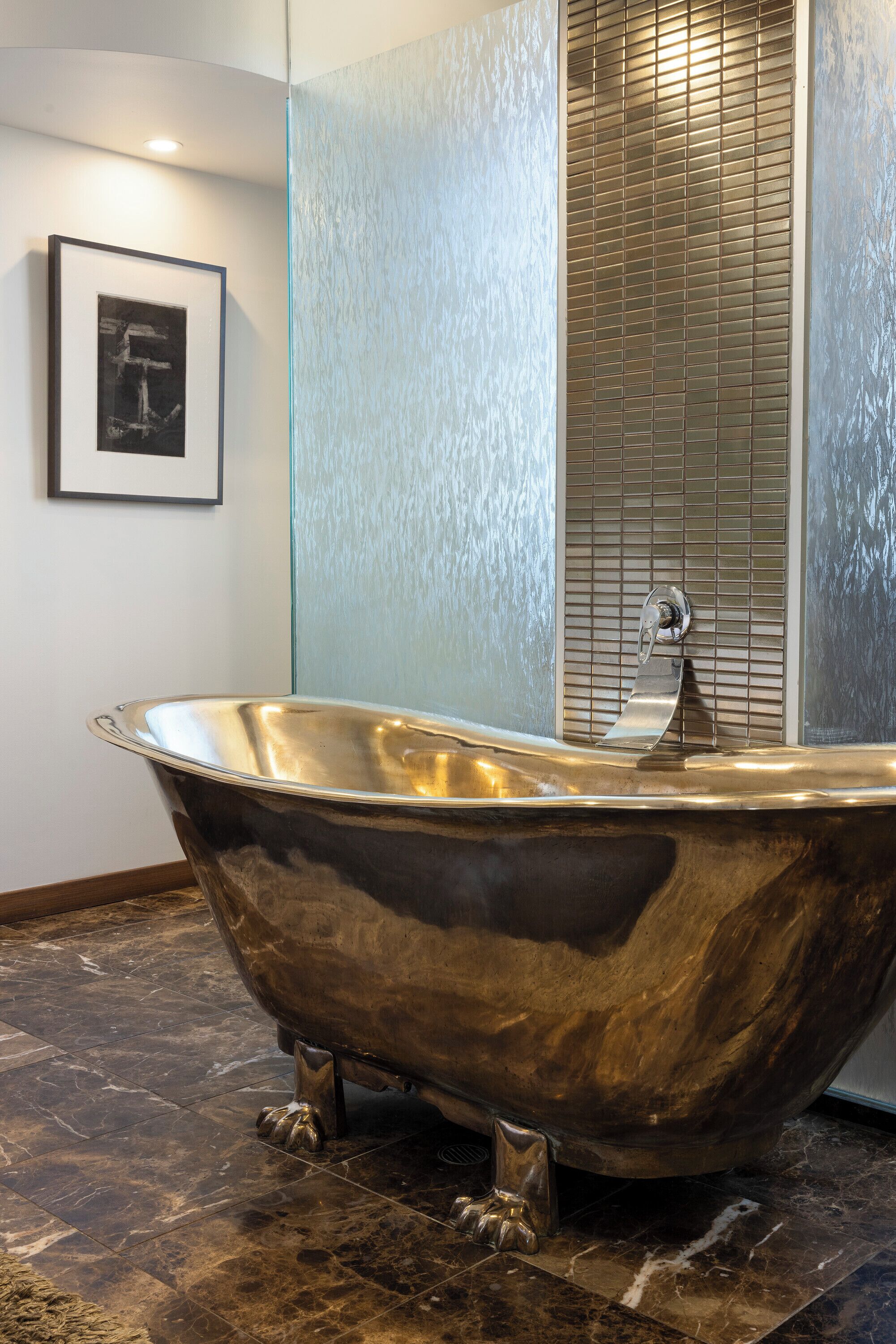 A large, freestanding bathtub in a modern bathroom with a textured wall and a framed picture on the wall.