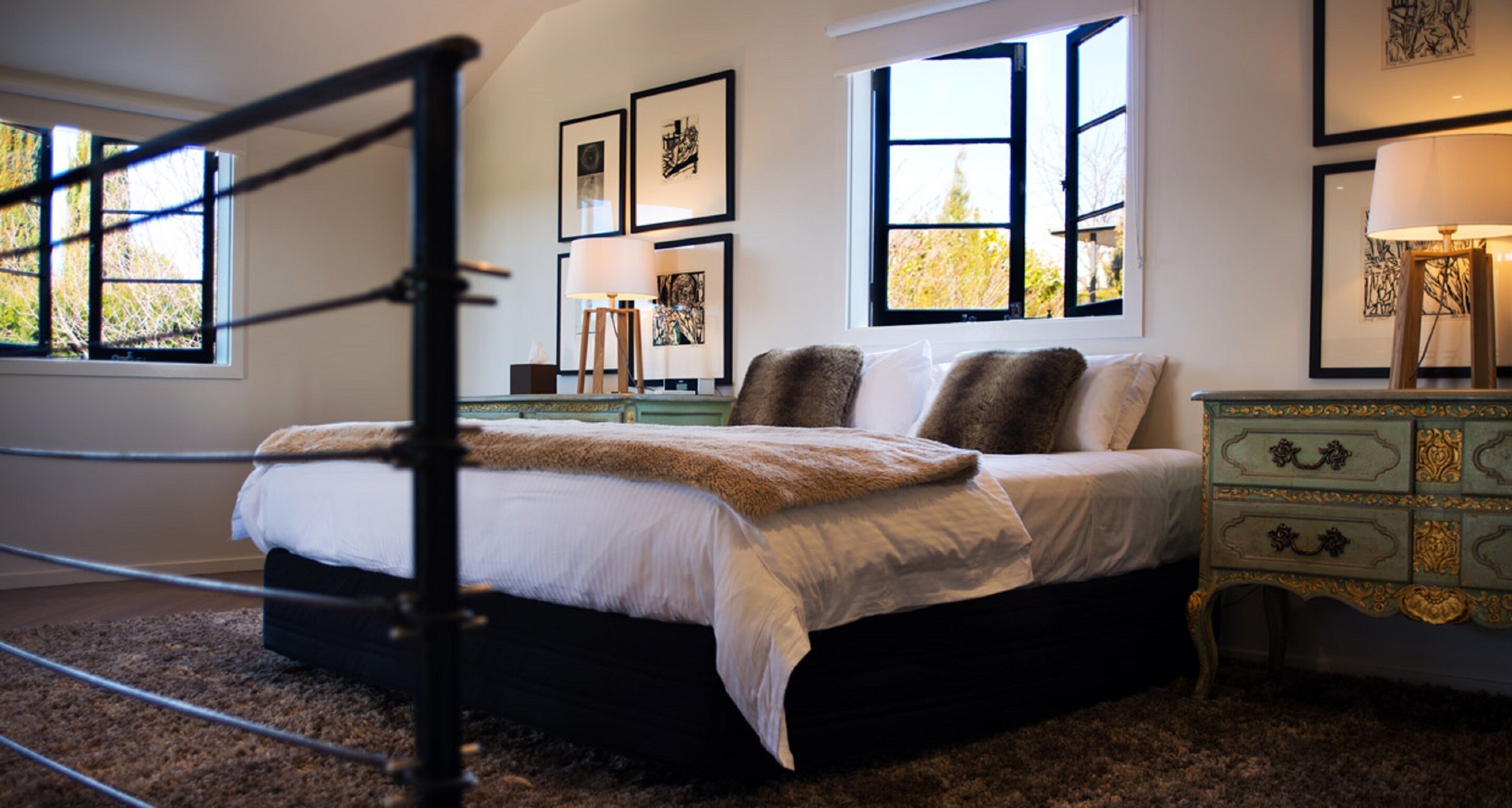 Ein Schlafzimmer mit Bett, Nachttisch, Lampe und gerahmten Kunstwerken an der Wand.