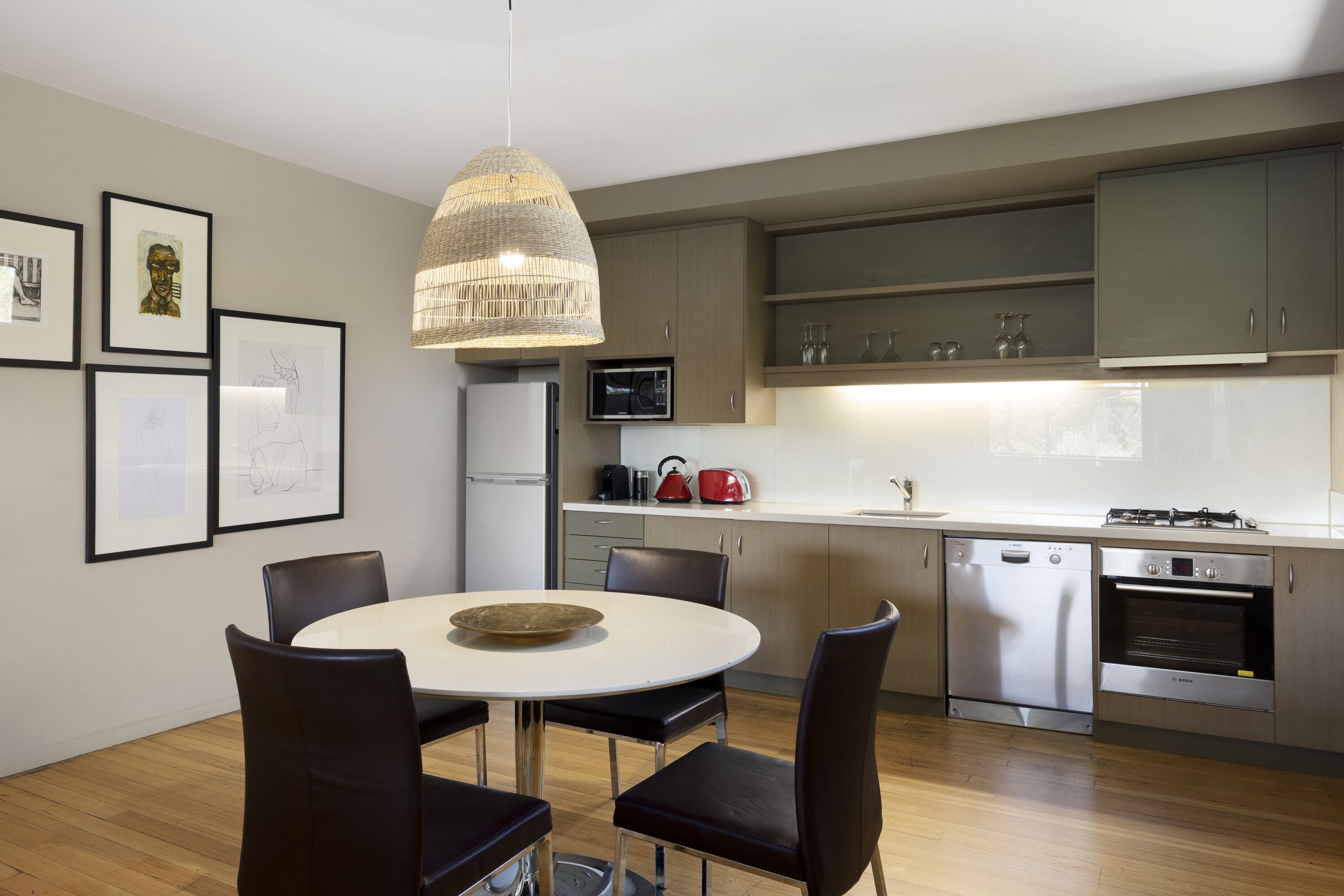 Una cocina moderna con comedor, que cuenta con electrodomésticos de acero inoxidable, armarios de madera y una lámpara colgante.