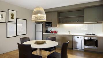 Una cocina moderna con comedor, que cuenta con electrodomésticos de acero inoxidable, armarios de madera y una lámpara colgante.