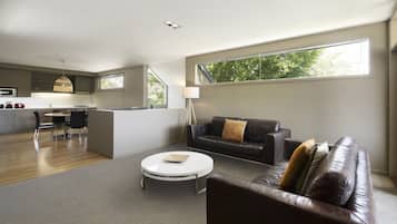 A modern living room with a leather sofa, a coffee table, and a dining area with a kitchen in the background.