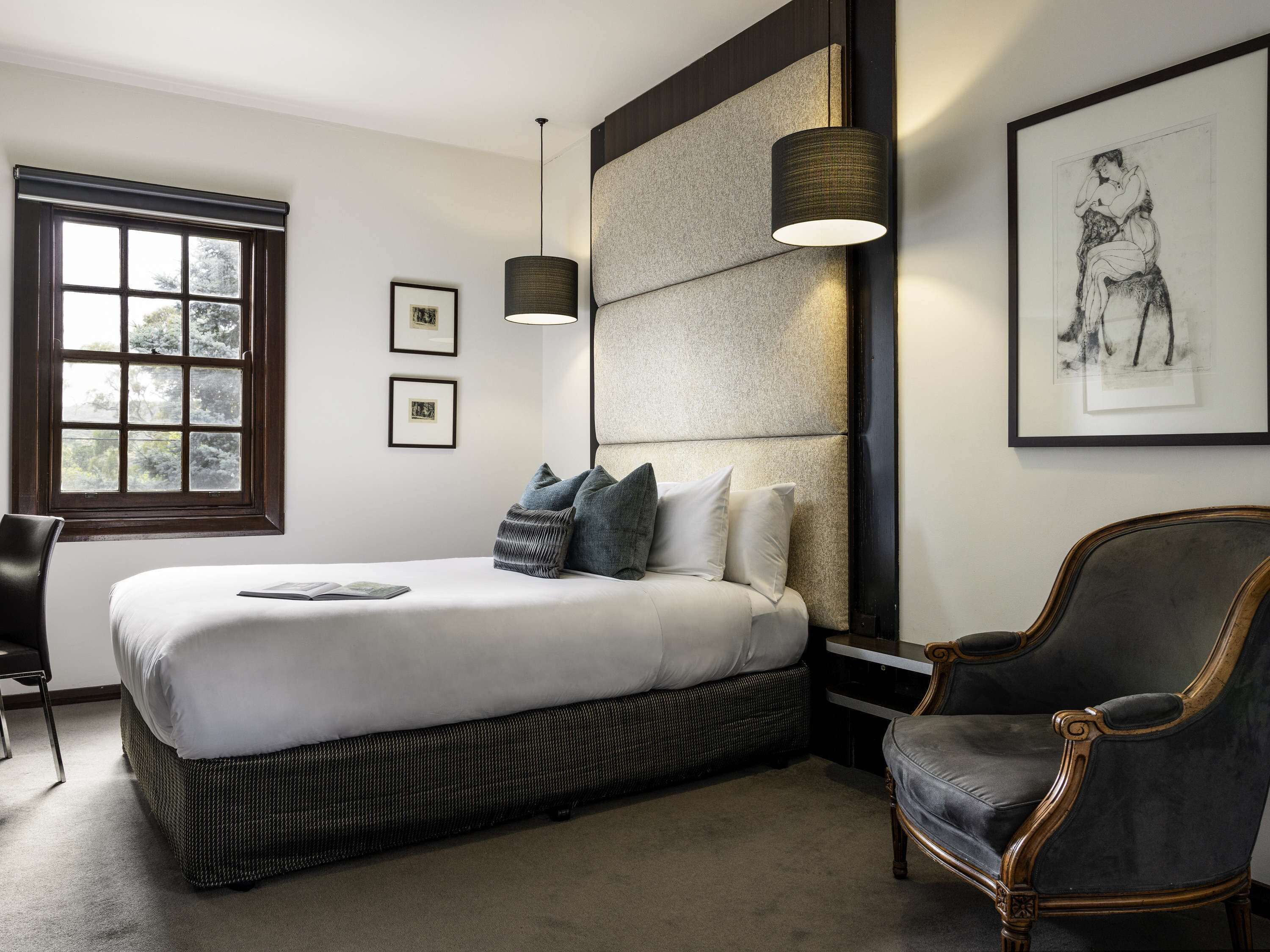 Un dormitorio moderno con una cama grande, una mesita de noche, una silla y una ventana con cuadros.