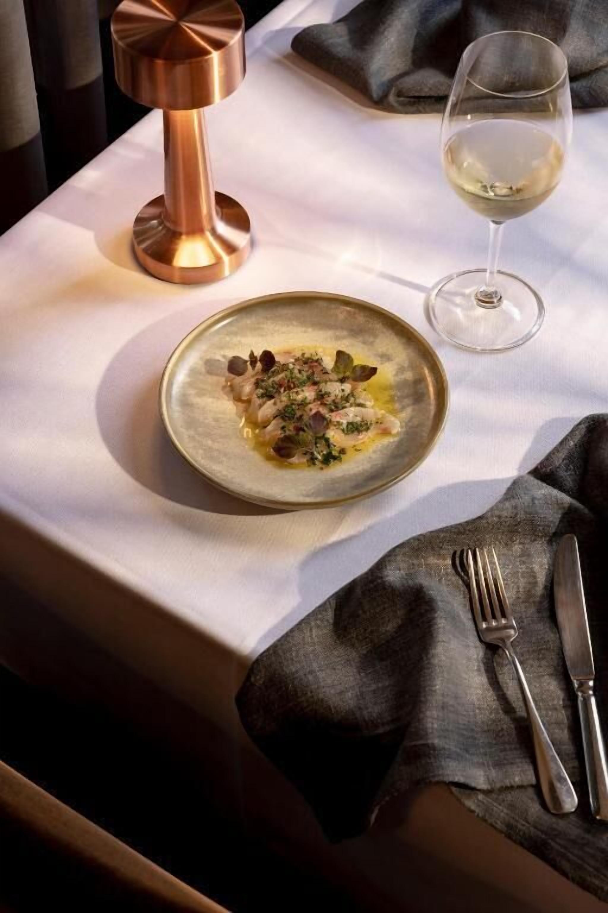 A table with a plate of food, a glass of white wine, and a copper candle holder.