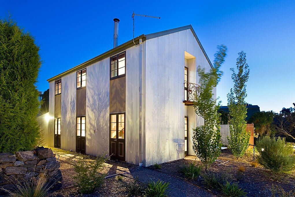 A modern, single-story building with a corrugated metal exterior, large windows, and a chimney.