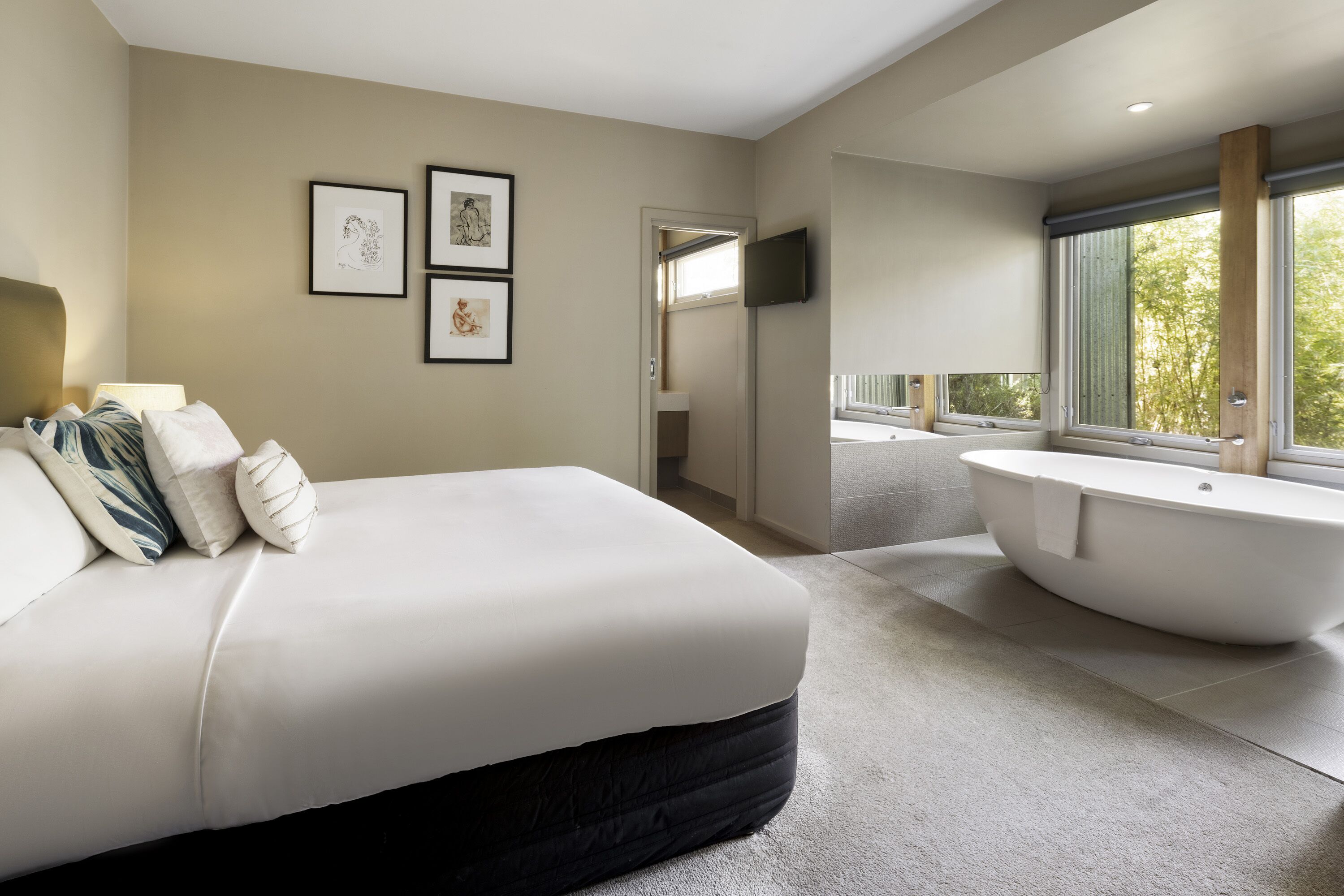 Ein modernes Schlafzimmer mit einem großen Bett, einer Badewanne und einem an der Wand montierten Fernseher.