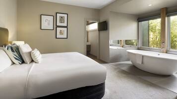 Un dormitorio moderno con una cama grande, una bañera y un televisor en la pared.
