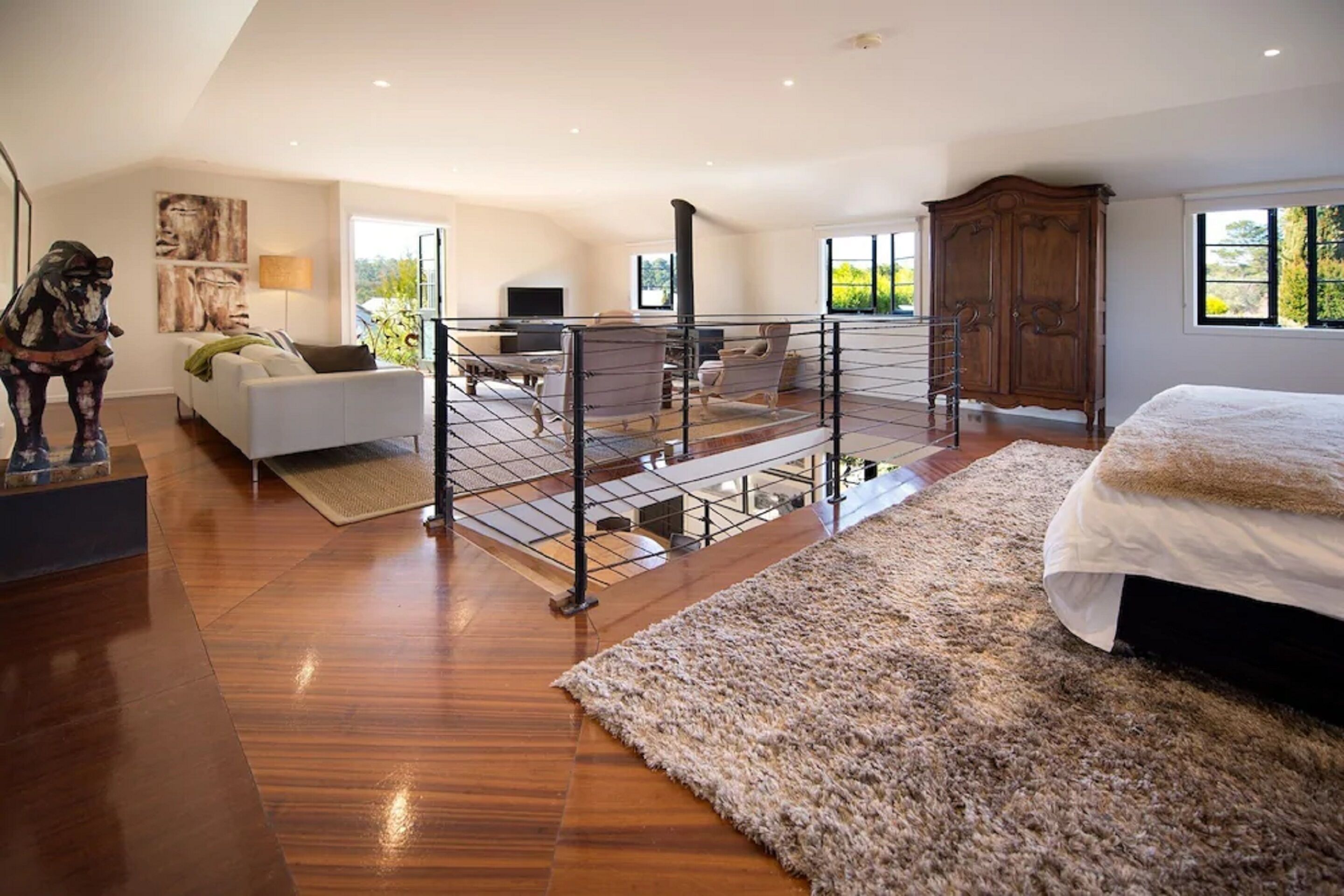 Une chambre spacieuse avec un grand lit, un plancher en bois, un balcon avec une balustrade et une vue sur la verdure environnante.