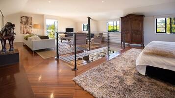 Une chambre spacieuse avec un grand lit, un plancher en bois, un balcon avec une balustrade et une vue sur la verdure environnante.