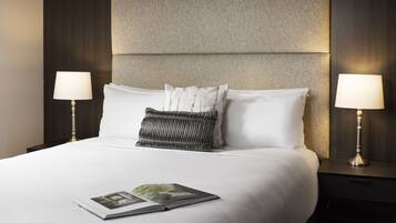 A neatly made bed with white linens, two bedside lamps, and a book on the bed.