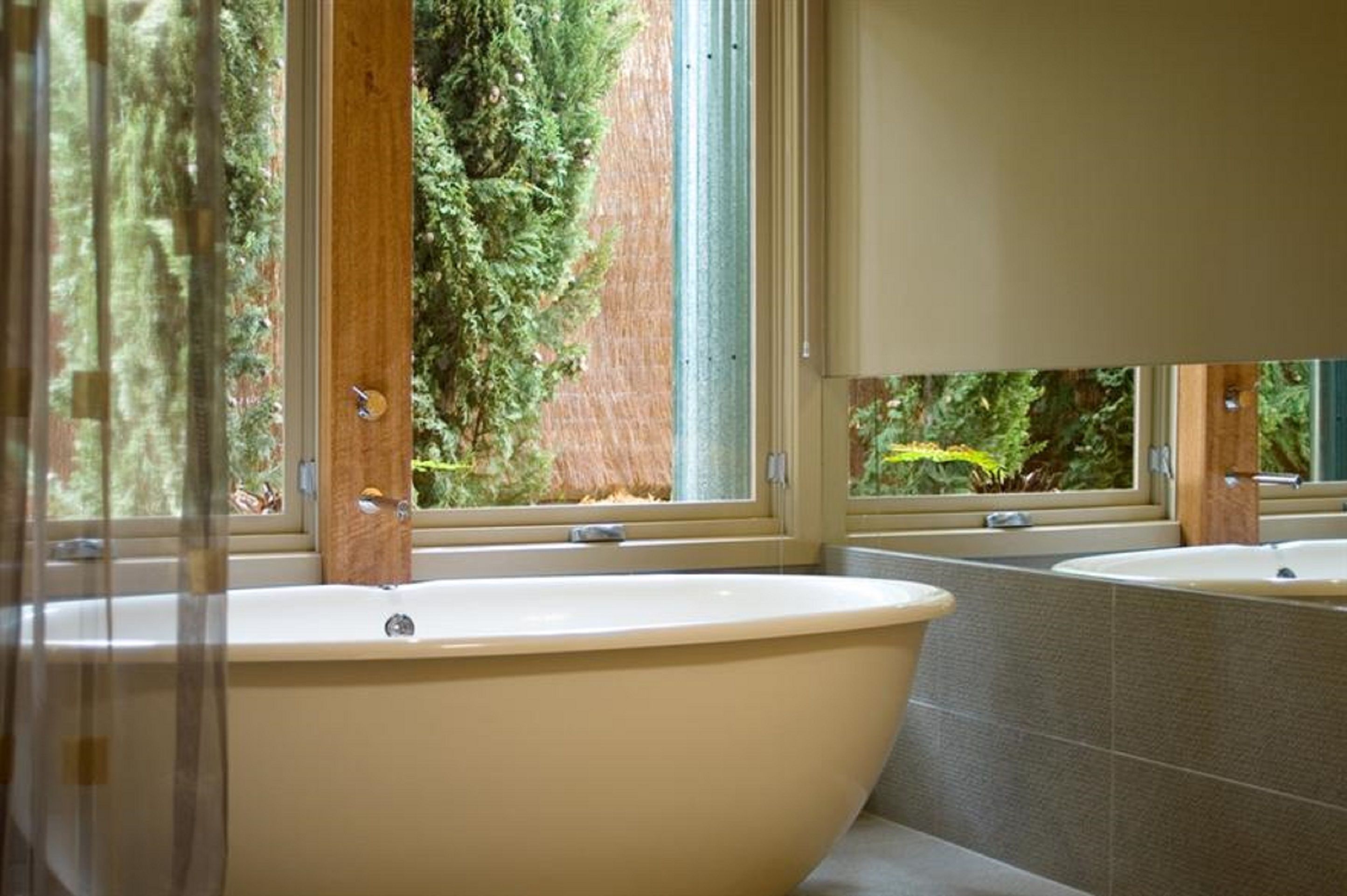 Un baño con una bañera independiente, un ventanal con vistas a árboles y una pared con azulejos.
