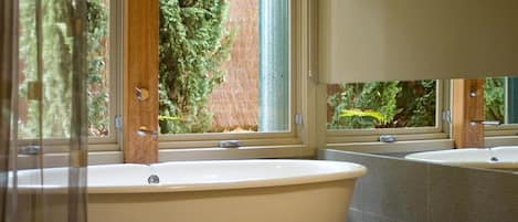 Un baño con una bañera independiente, un ventanal con vistas a árboles y una pared con azulejos.
