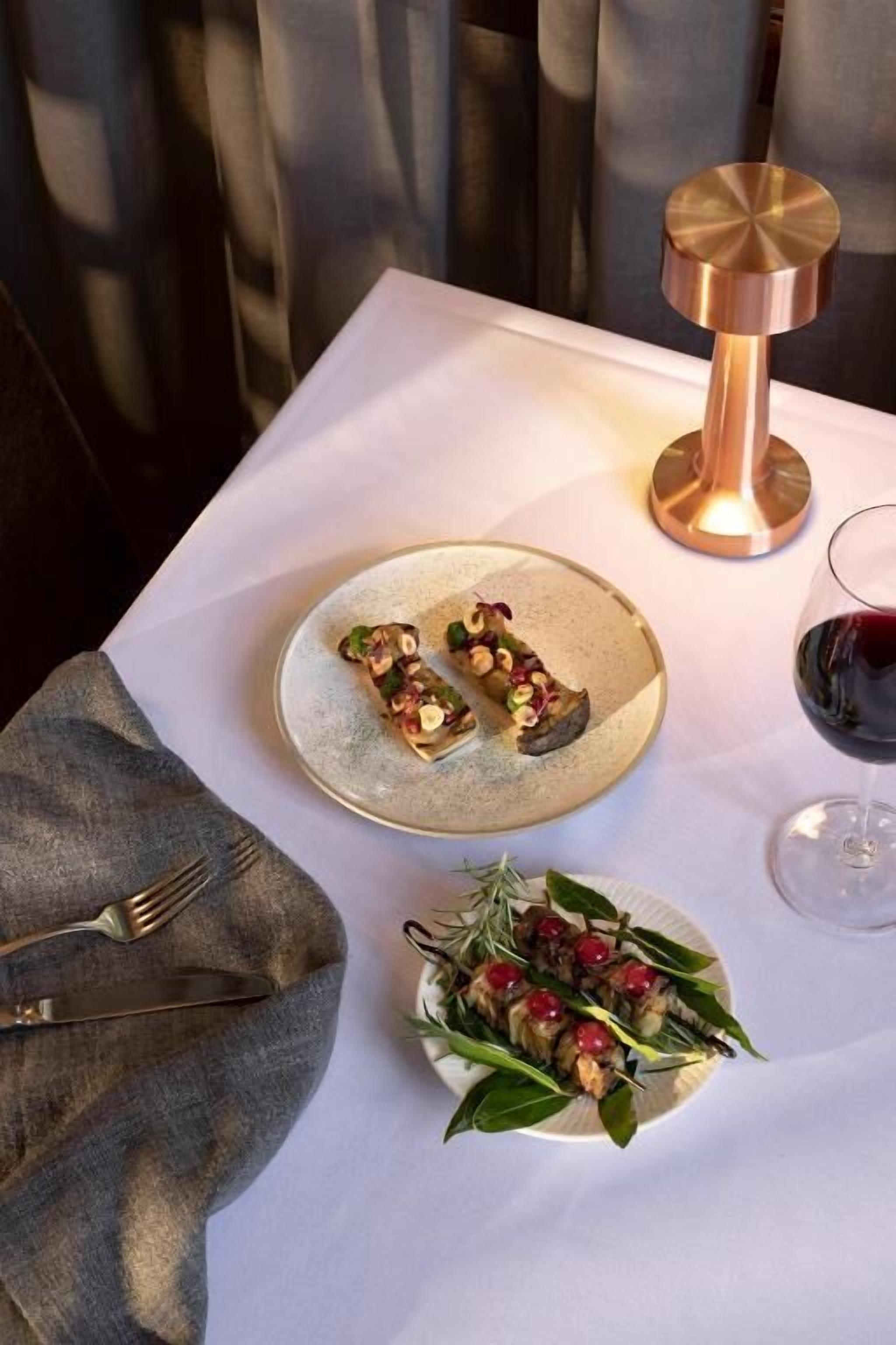 Een tafel met een bord eten, een glas rode wijn en een kaars.