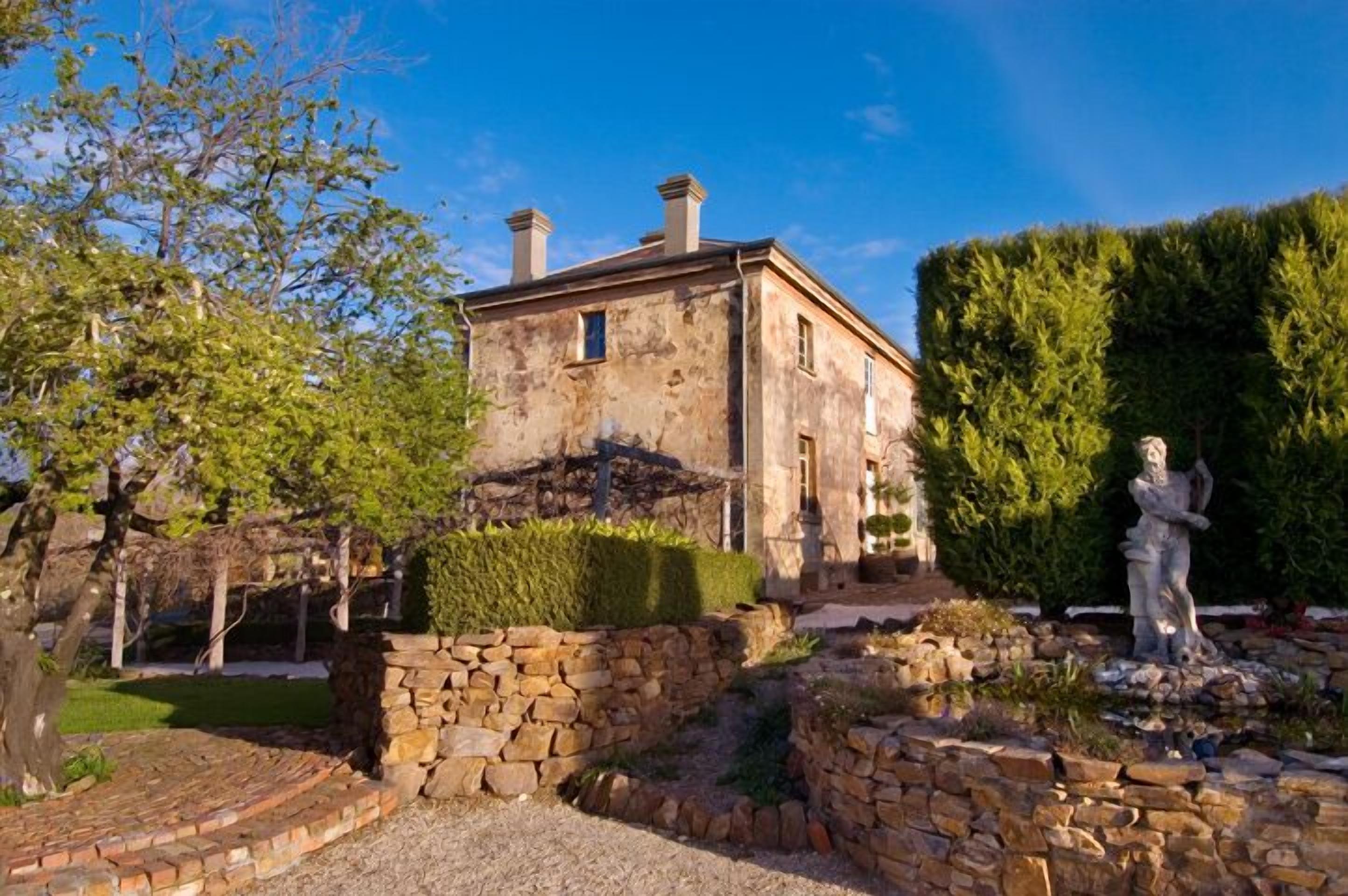 A stone building with a garden, including a statue and well-maintained hedges.