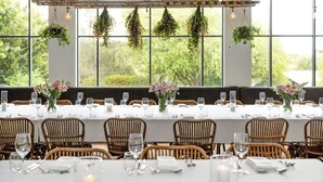 A dining area with tables set for six, large windows, and hanging plants. - Mineral Springs Hotel (Hepburn Springs)