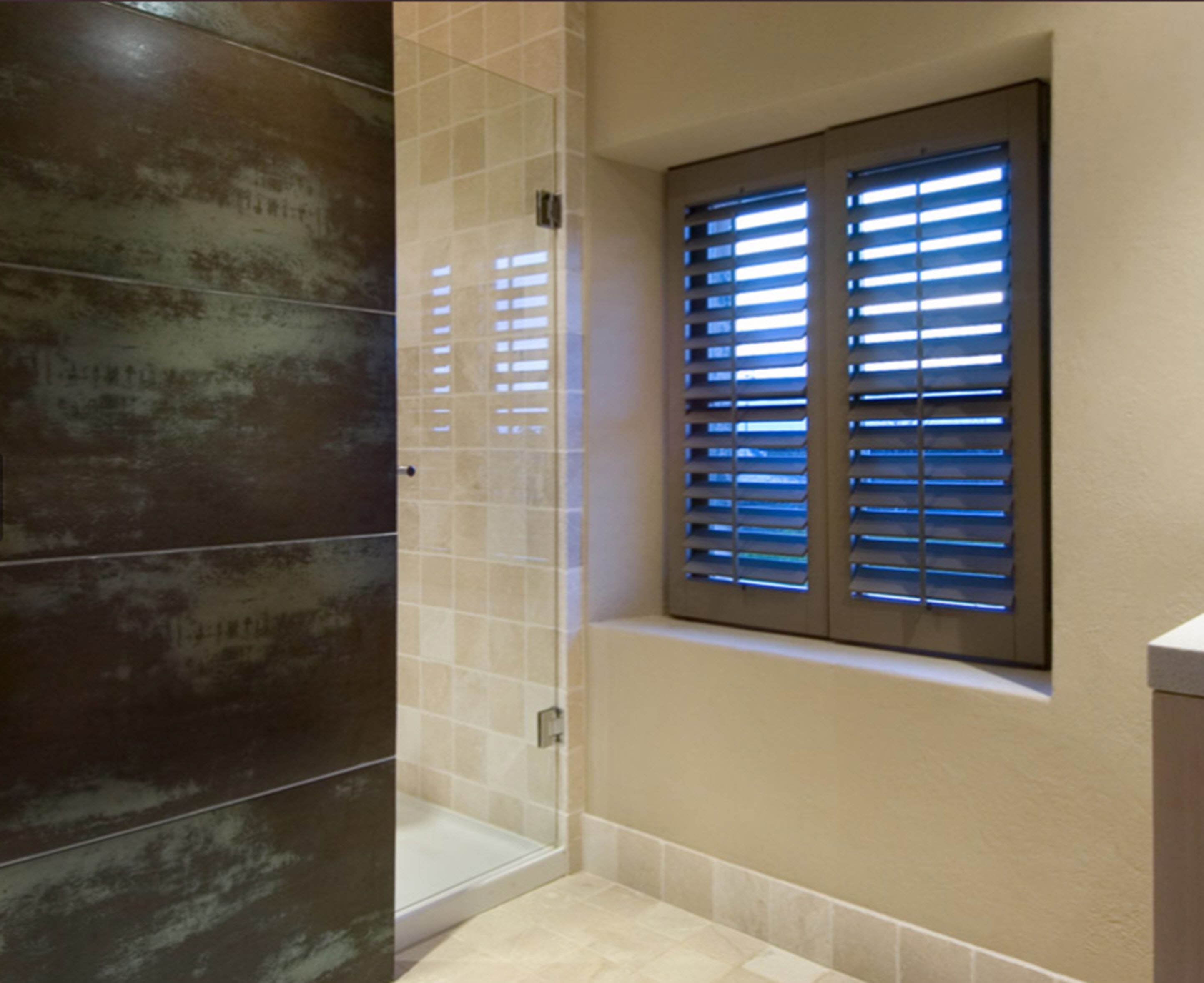 A bathroom with a glass shower enclosure, a window with blinds, and a tiled floor.