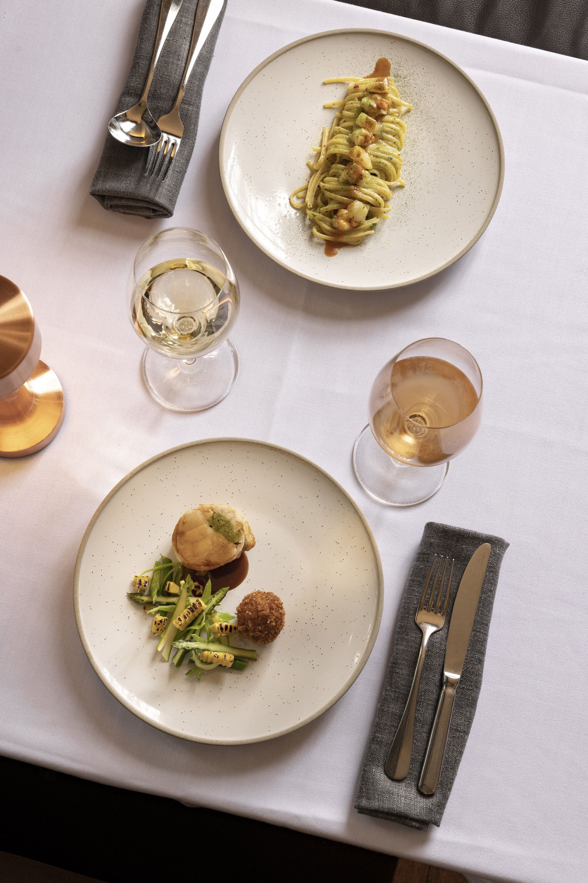 A table set with plates of food, glasses of wine, and cutlery.