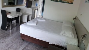 Quarto de hotel com cama, escrivaninha, cadeira, espelho e um quadro na parede.