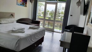 Quarto de hotel com cama, escrivaninha, cadeira, varanda e uma vista, além de um quadro na parede.