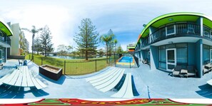 A modern building with a curved facade, outdoor seating, and a pool area. - Le George Motel (Port Macquarie)