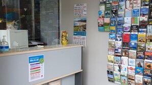 Bancada de recepção com computador, relógio e um mural repleto de folhetos.