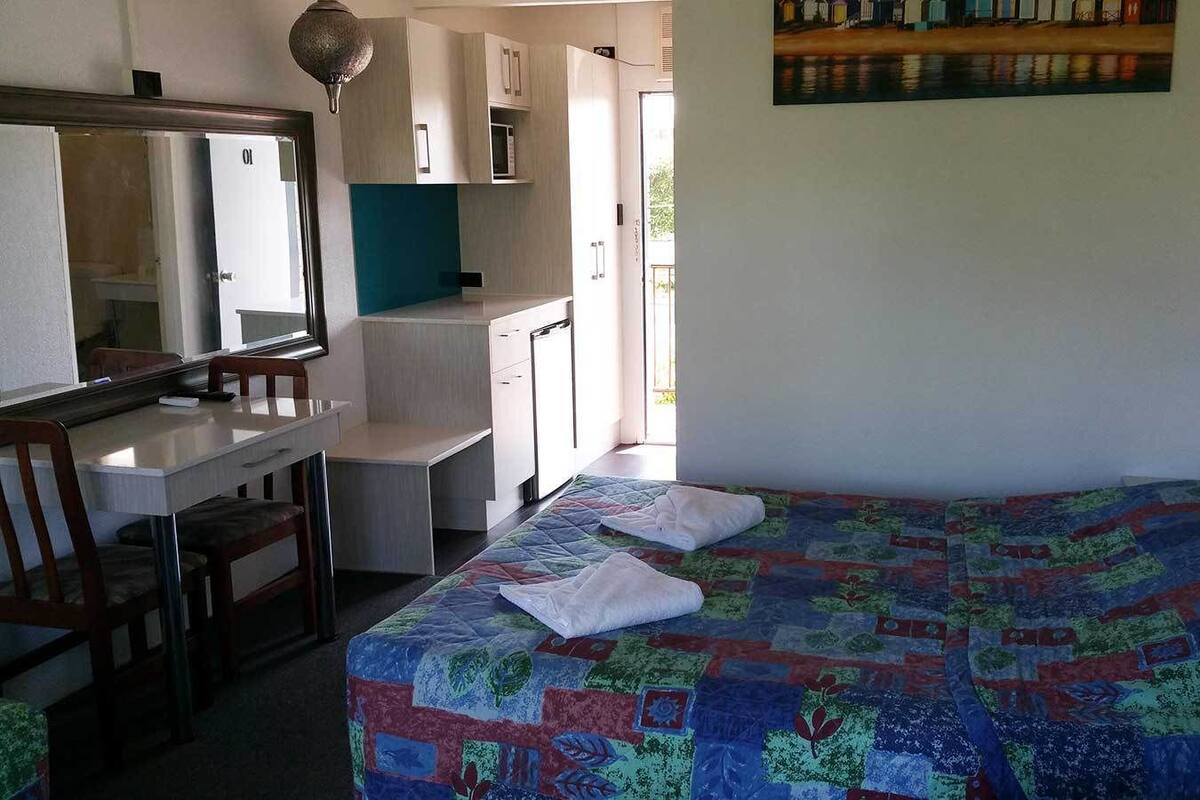 A bedroom with a bed, a desk, and a chair. There is a window with a view of a building outside.