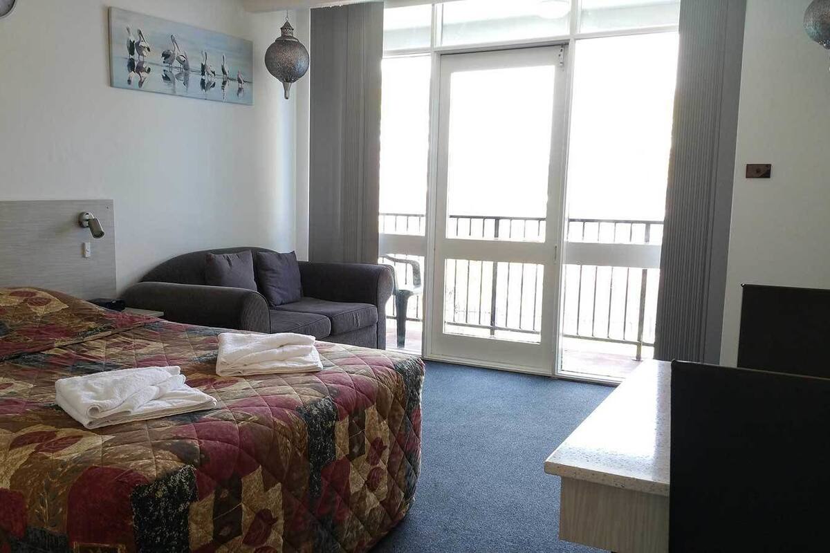 A hotel room with a large bed, a desk, a chair, and a balcony with a view.