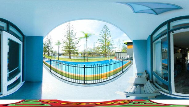 Vista circular de uma área de piscina com cerca, árvores e um edifício ao fundo.