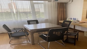 Una habitación con una mesa y cuatro sillas, un escritorio con una computadora y una ventana con cortinas.