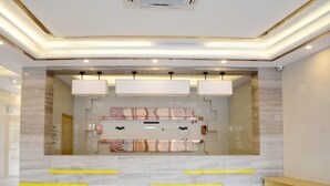 Zona de recepción con suelo de mármol, mostrador de recepción y área de estar con tapicería estampada.