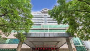 A multi-story hotel with a modern architectural design, featuring a prominent entrance with glass doors and a red sign. - Grand Hotel Yuanshan (Beijing)