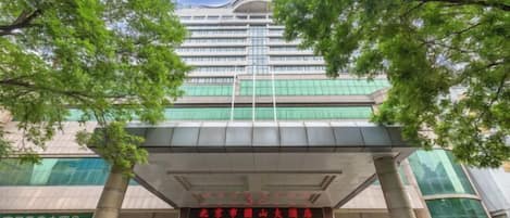 Un hotel de varios pisos con un diseño arquitectónico moderno, que presenta una entrada destacada con puertas de cristal y un letrero rojo.