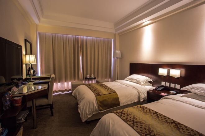 Ein Hotelzimmer mit zwei Betten, einem Schreibtisch, einem Stuhl, einer Lampe, einem Telefon und einem Fenster mit Vorhängen.