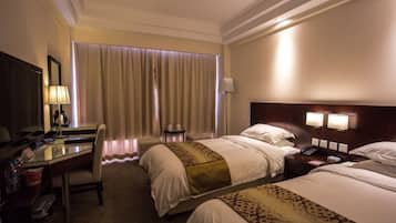 Ein Hotelzimmer mit zwei Betten, einem Schreibtisch, einem Stuhl, einer Lampe, einem Telefon und einem Fenster mit Vorhängen.