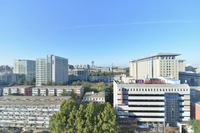 A cityscape with various buildings, including a large multi-story structure with a flat roof and a smaller building with a sloped roof.