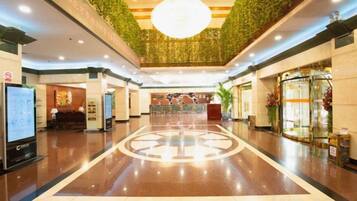A hotel lobby with a reception desk, a digital information kiosk, and a decorative ceiling.