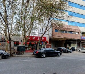 Vista de la calle con coches aparcados, un edificio con toldo rojo y un árbol en primer plano.