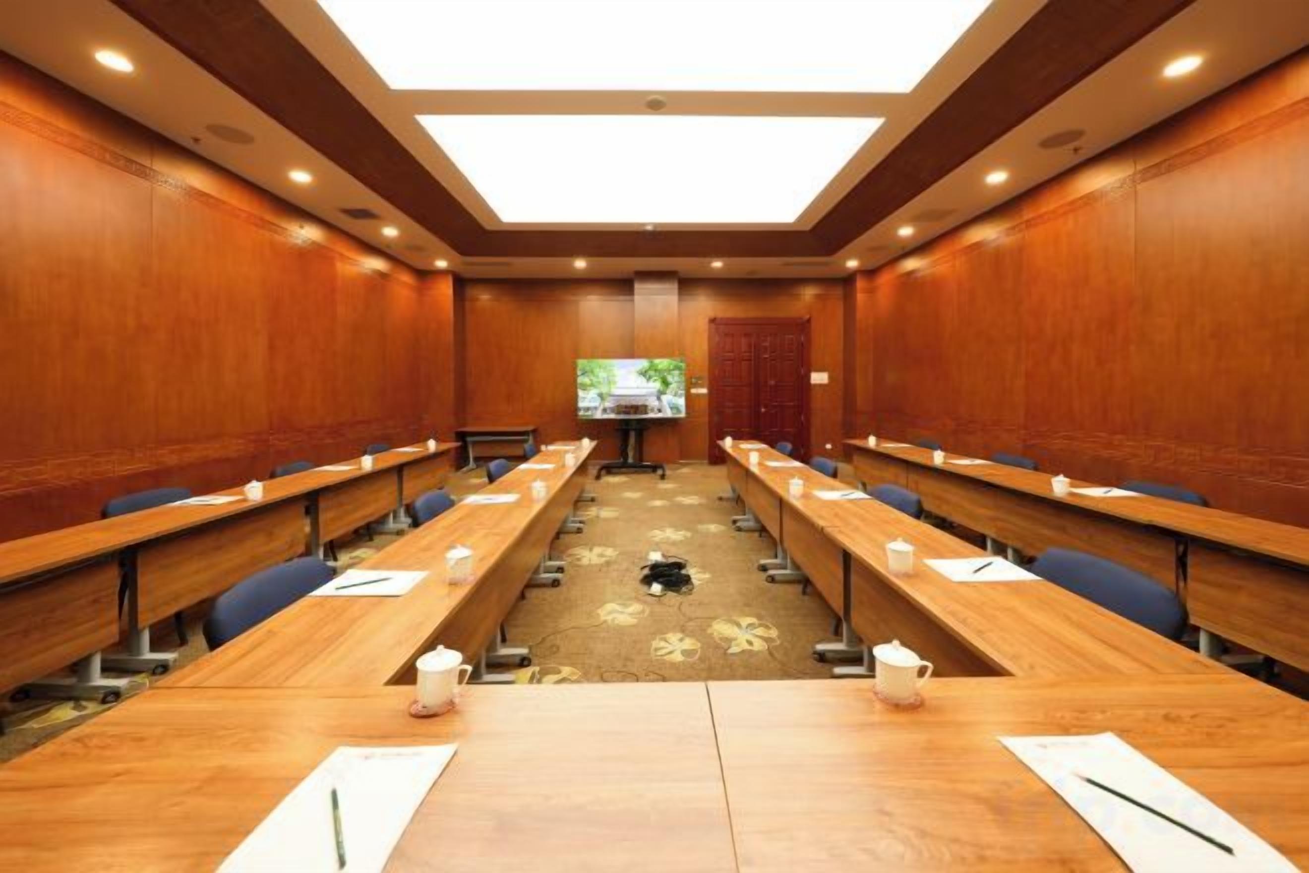 Een congreszaal met lange tafels, stoelen en een groot scherm aan de voorkant.