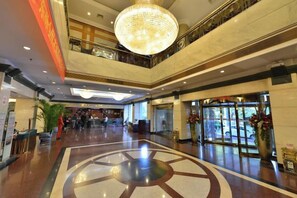 Un vestíbulo de hotel con una gran araña, un mostrador de recepción y un diseño decorativo en el suelo.